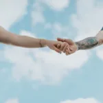 Kaksi ihmistä pitää toisiaan kädestä taivasta vasten