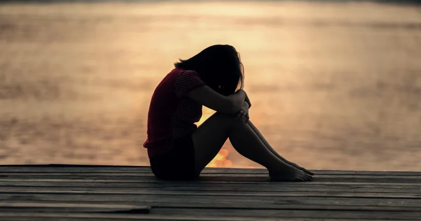 Nainen istuu laiturilla polvet koukussa auringonlaskussa
